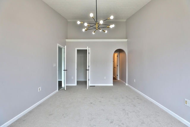 carpeted empty room featuring arched walkways, baseboards, a notable chandelier, and a towering ceiling