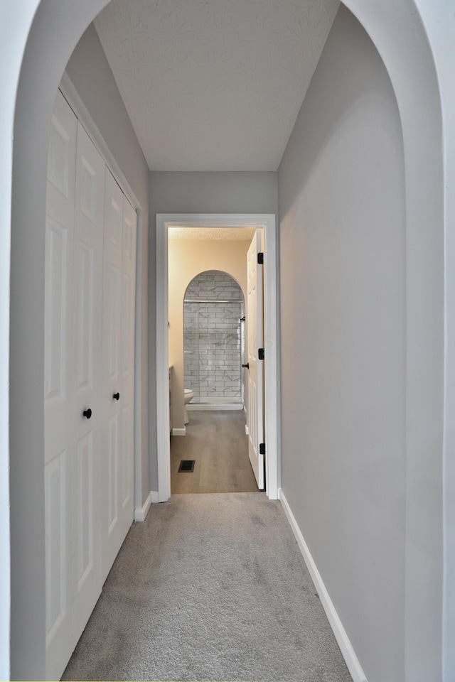 hall featuring baseboards, carpet flooring, arched walkways, and visible vents