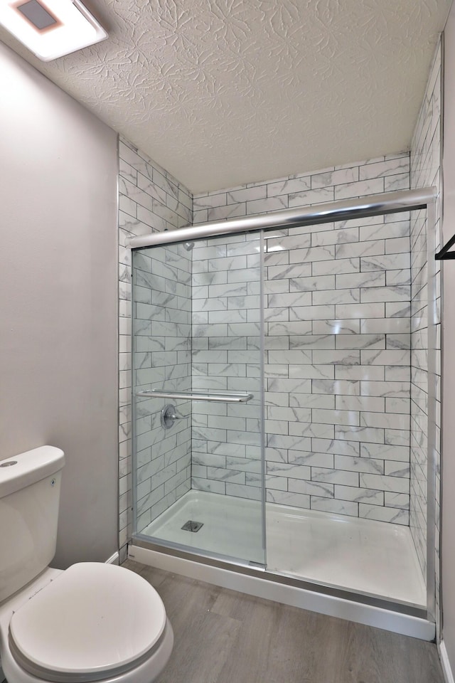 full bathroom featuring toilet, a textured ceiling, a shower stall, and wood finished floors