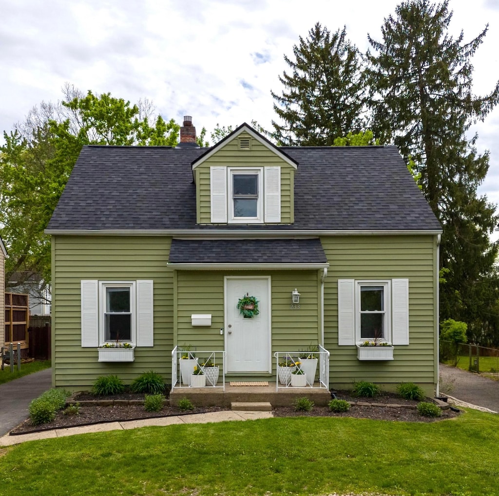 new england style home with a shingled roof and a front lawn