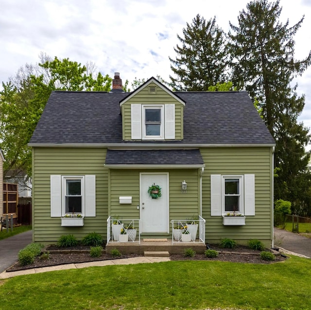 new england style home with a shingled roof and a front lawn