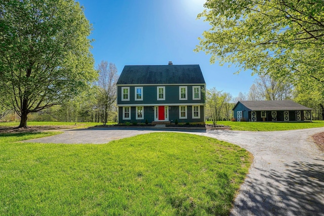 colonial house with curved driveway, a chimney, and a front yard