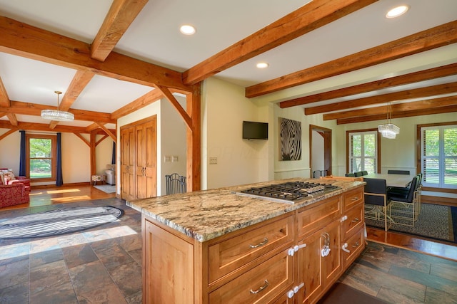 kitchen with beamed ceiling, open floor plan, light stone countertops, and stainless steel gas stovetop