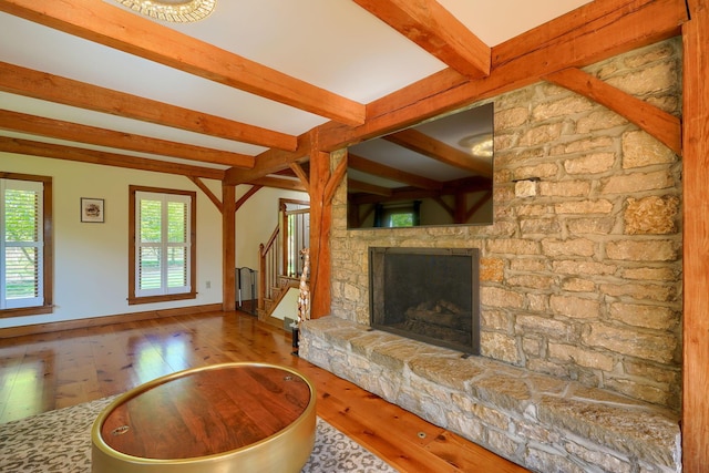 unfurnished living room with a stone fireplace, stairway, hardwood / wood-style floors, and beamed ceiling