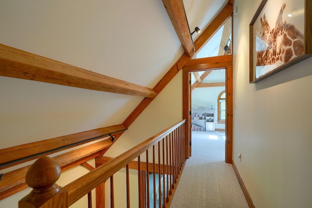 hallway with carpet floors, lofted ceiling with beams, baseboards, and an upstairs landing