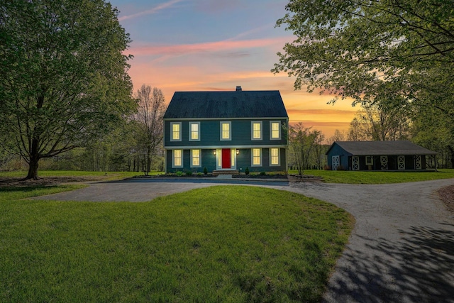 view of front of house with curved driveway, a chimney, and a yard
