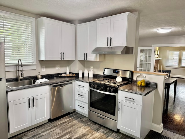 1464 E 26th Ave, Columbus, OH 43211 - kitchen with appliances with stainless steel finishes, under cabinet range hood, dark countertops, a sink, and a textured ceiling