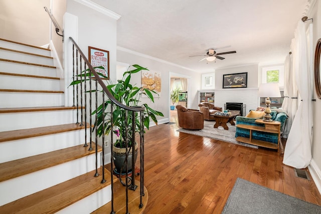 living room featuring crown molding, visible vents, stairs, wood finished floors, and ceiling fan