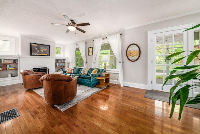 living area featuring a fireplace, a ceiling fan, crown molding, and hardwood / wood-style floors