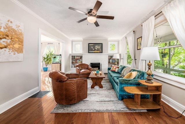 living area featuring a ceiling fan, a fireplace, baseboards, wood-type flooring, and ornamental molding