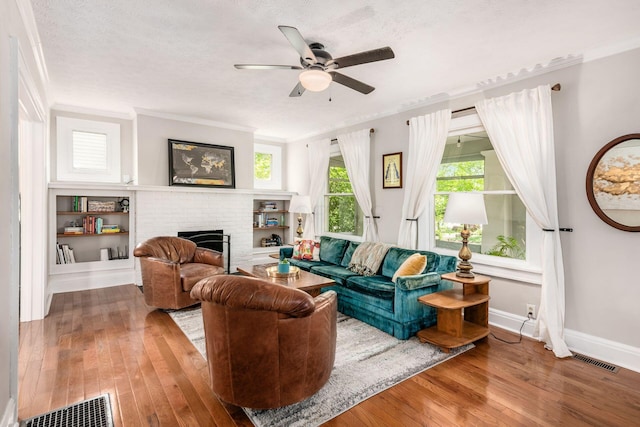 living area featuring crown molding, wood-type flooring, a brick fireplace, a ceiling fan, and visible vents