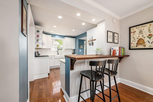 kitchen with a breakfast bar area, white cabinets, dark wood-style floors, and a sink