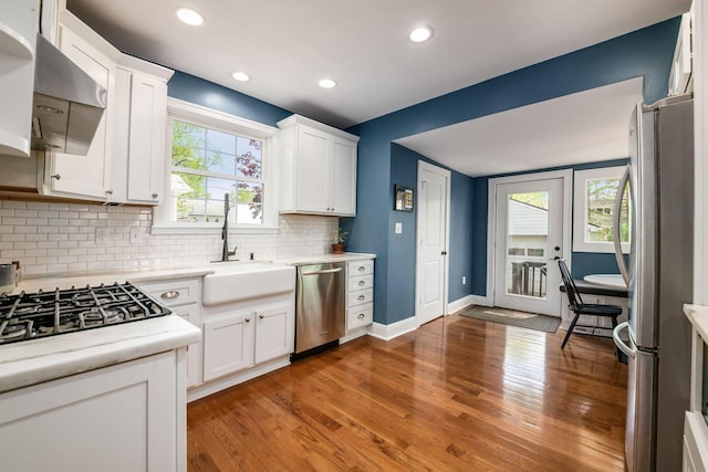 kitchen featuring appliances with stainless steel finishes, tasteful backsplash, a sink, light wood finished floors, and white cabinetry