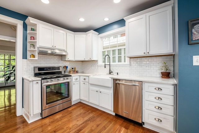 kitchen featuring appliances with stainless steel finishes, light wood-type flooring, a sink, under cabinet range hood, and white cabinetry