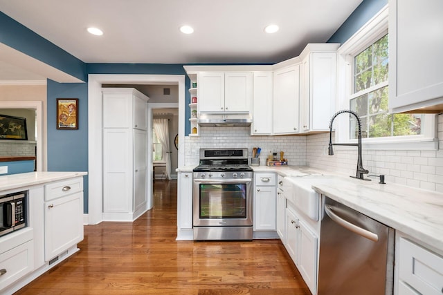 kitchen featuring appliances with stainless steel finishes, tasteful backsplash, a sink, white cabinets, and under cabinet range hood