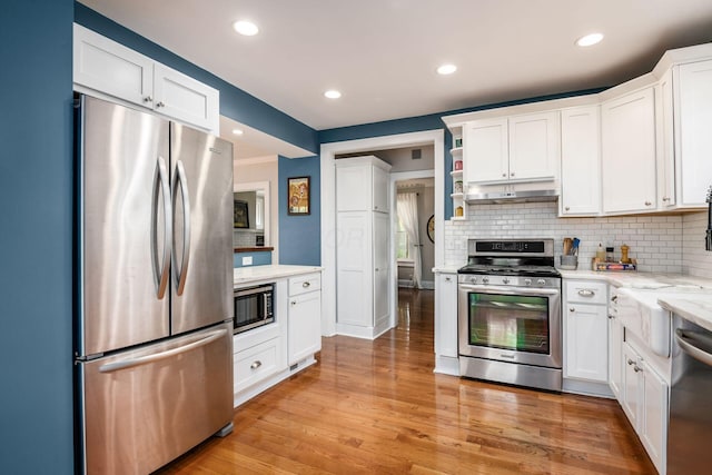 kitchen with tasteful backsplash, stainless steel appliances, white cabinets, and under cabinet range hood