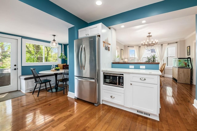 kitchen with visible vents, appliances with stainless steel finishes, white cabinets, light wood finished floors, and an inviting chandelier