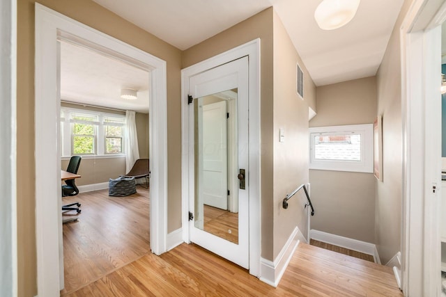 hall featuring light wood-style floors, baseboards, and visible vents