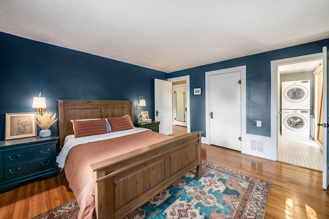 bedroom with baseboards, visible vents, wood finished floors, and stacked washer and clothes dryer