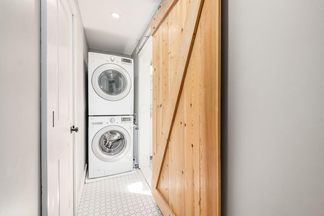 laundry room with laundry area, a barn door, stacked washing maching and dryer, tile patterned floors, and recessed lighting