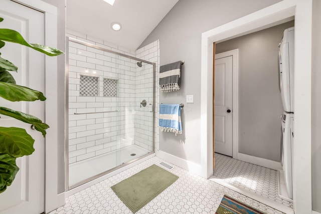 bathroom with stacked washer and dryer, visible vents, a shower stall, vaulted ceiling, and baseboards