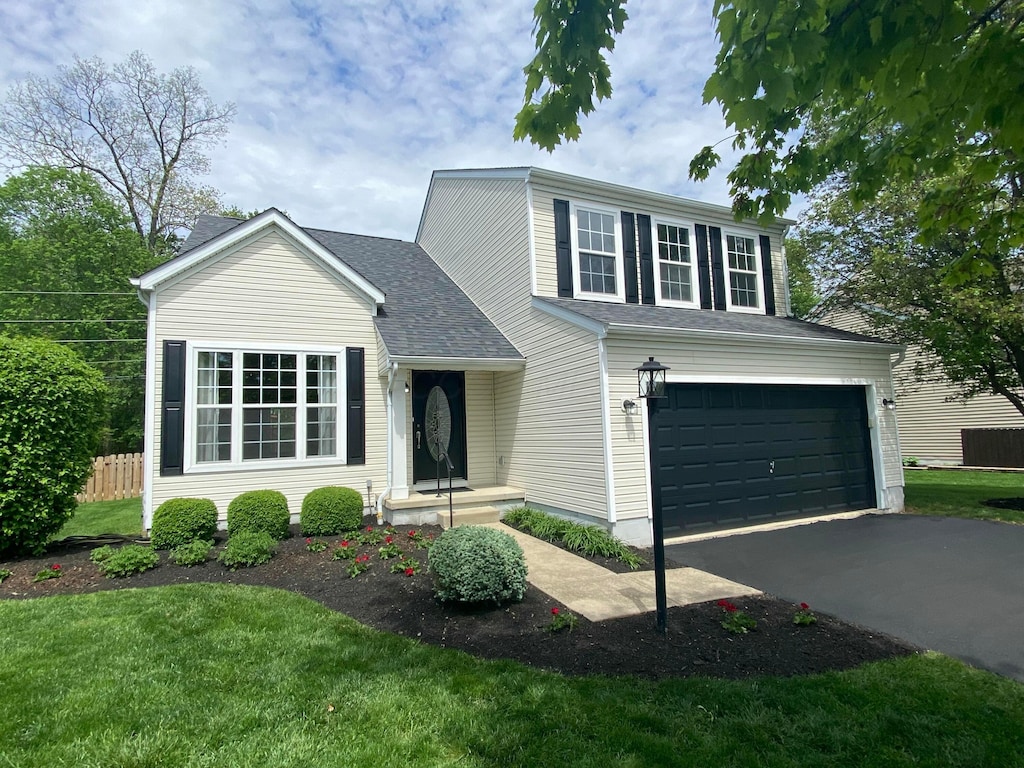 traditional-style home featuring fence, an attached garage, a front lawn, and aphalt driveway