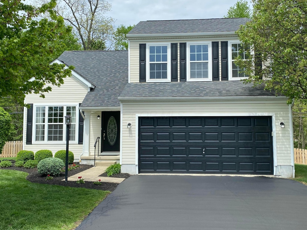 traditional-style house featuring fence, an attached garage, roof with shingles, and aphalt driveway