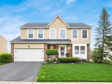 traditional-style home with an attached garage, stucco siding, driveway, and a front lawn