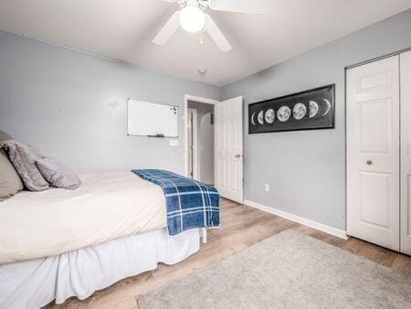 bedroom with baseboards, ceiling fan, wood finished floors, and a closet