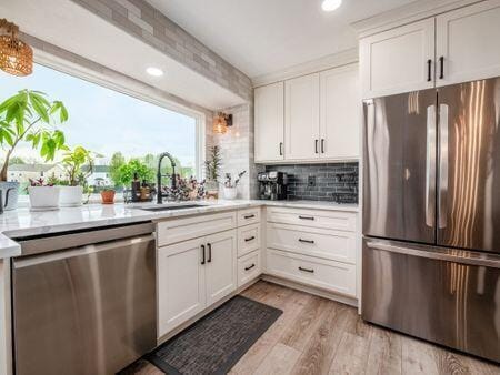 kitchen featuring appliances with stainless steel finishes, a sink, light countertops, white cabinets, and light wood finished floors