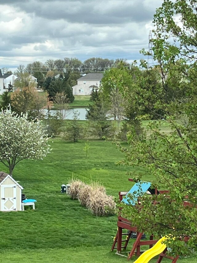 view of home's community featuring an outdoor structure, a playground, a storage unit, a yard, and a water view
