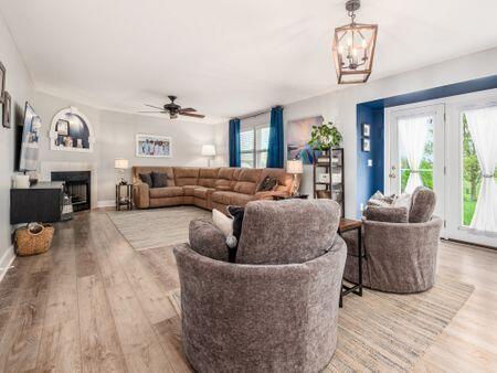 living room with baseboards, wood finished floors, ceiling fan with notable chandelier, and a fireplace