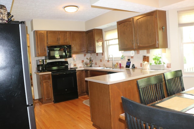 10160 Wellington Dr, Pickerington, OH 43147 - kitchen featuring a sink, light wood finished floors, a peninsula, backsplash, and black appliances