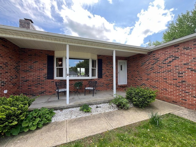 view of exterior entry with brick siding, covered porch, and a chimney