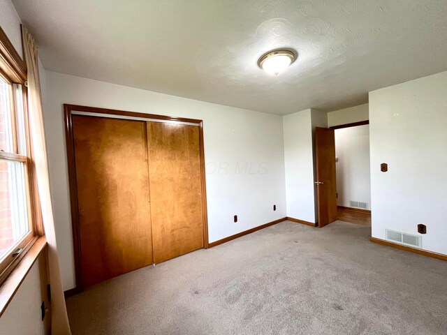 unfurnished bedroom with baseboards, carpet, a closet, and visible vents