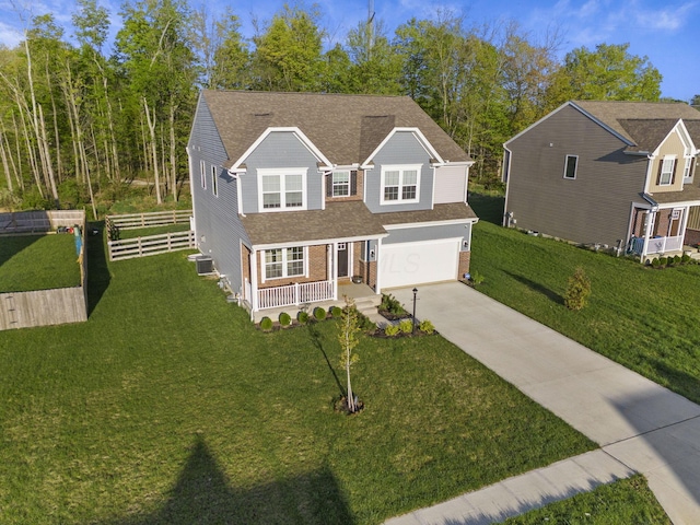 traditional-style house featuring fence, covered porch, a front yard, an attached garage, and driveway