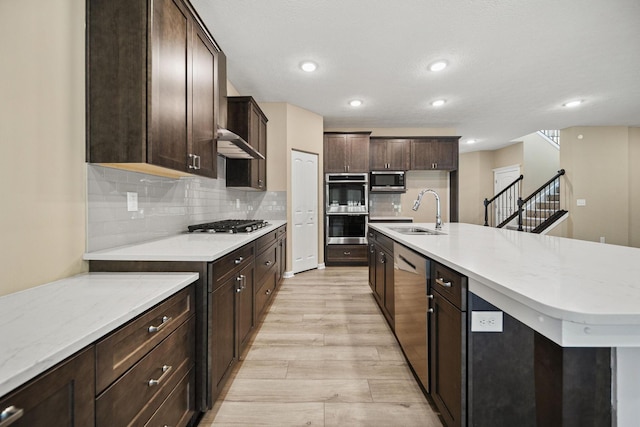 kitchen with dark brown cabinetry, tasteful backsplash, a sink, light wood-style flooring, and appliances with stainless steel finishes