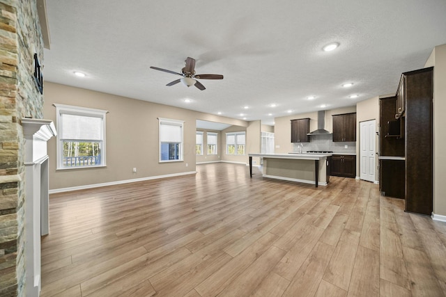 unfurnished living room with a ceiling fan, baseboards, a stone fireplace, and light wood-style floors