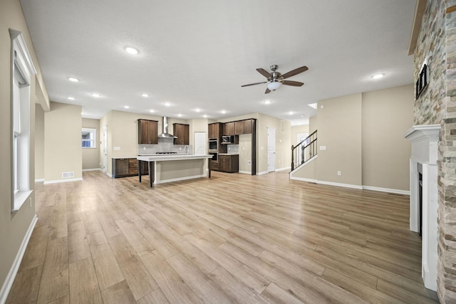 unfurnished living room featuring a ceiling fan, visible vents, light wood finished floors, and a fireplace