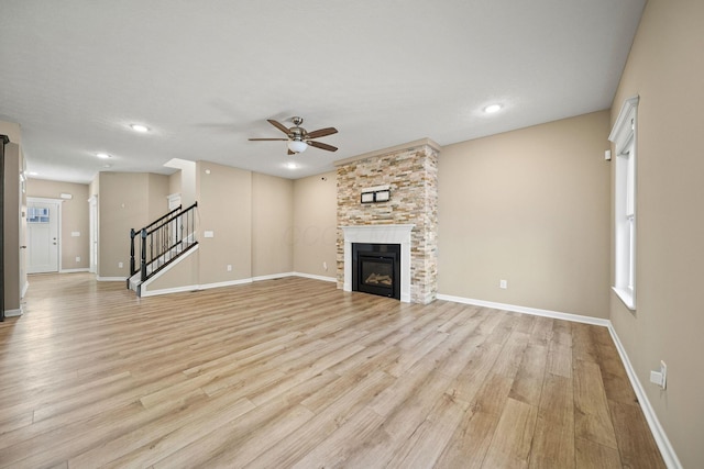 unfurnished living room featuring a glass covered fireplace, baseboards, stairway, a ceiling fan, and light wood finished floors