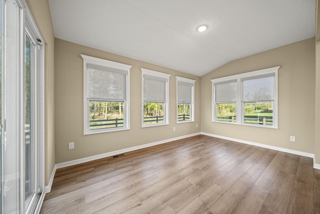 unfurnished room with baseboards, visible vents, wood finished floors, and lofted ceiling