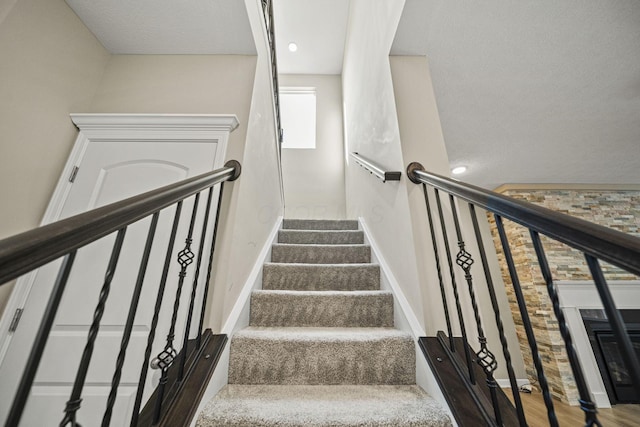 stairs featuring a glass covered fireplace, baseboards, and wood finished floors