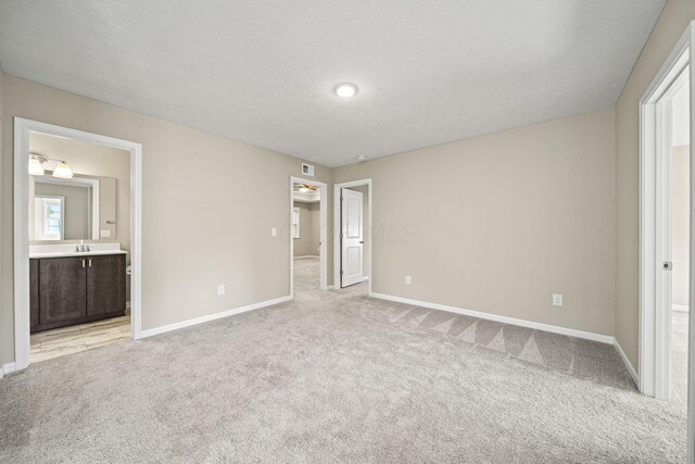 unfurnished bedroom featuring a sink, baseboards, light carpet, and visible vents
