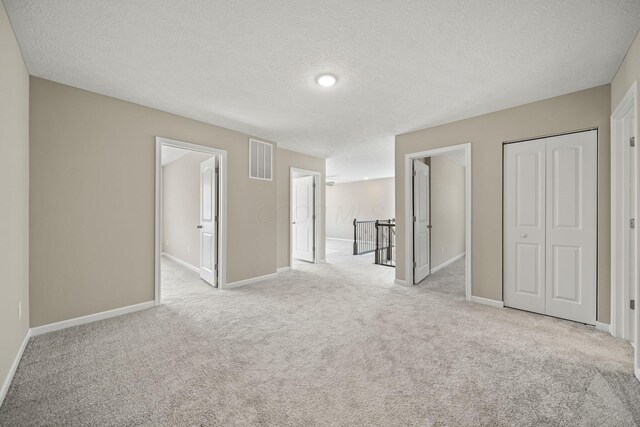 spare room with carpet flooring, a textured ceiling, visible vents, and baseboards