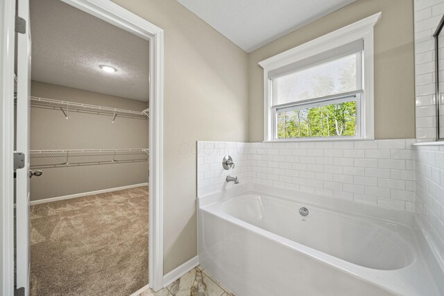 bathroom featuring a textured ceiling, baseboards, a spacious closet, and a bath