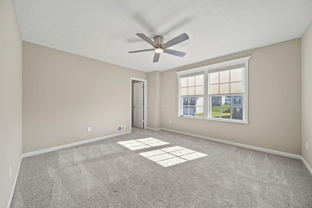 carpeted spare room featuring baseboards, a ceiling fan, a textured ceiling, and visible vents