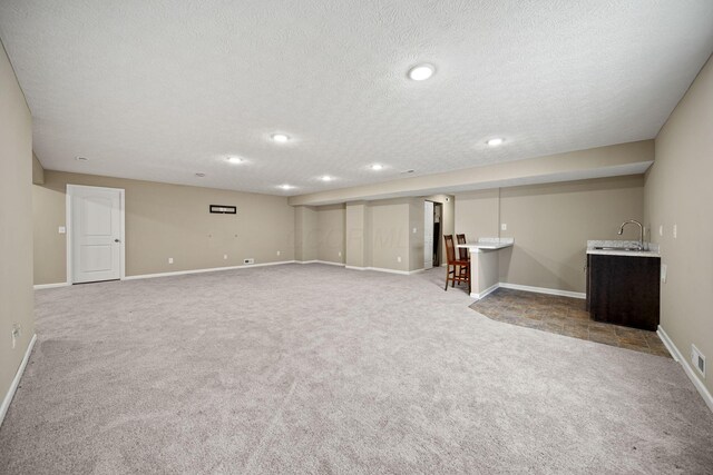 finished below grade area with a textured ceiling, a sink, carpet floors, baseboards, and indoor wet bar