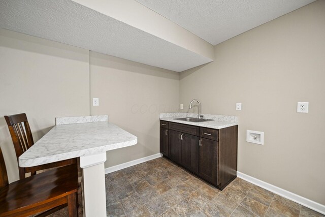 laundry area with stone finish floor, washer hookup, a textured ceiling, a sink, and baseboards