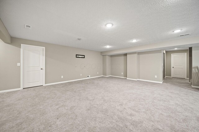 finished below grade area featuring carpet flooring, a textured ceiling, visible vents, and baseboards