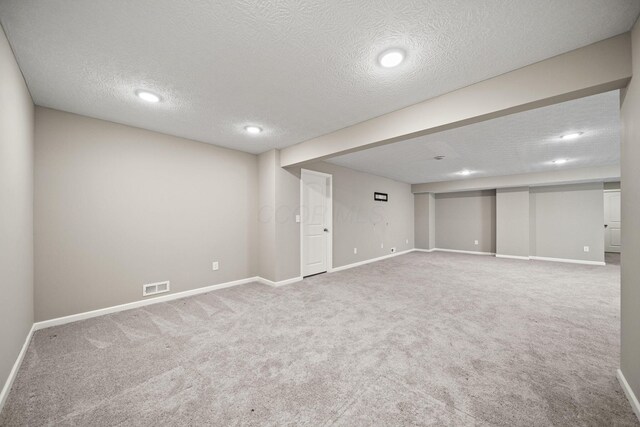 finished basement featuring visible vents, carpet flooring, a textured ceiling, and baseboards